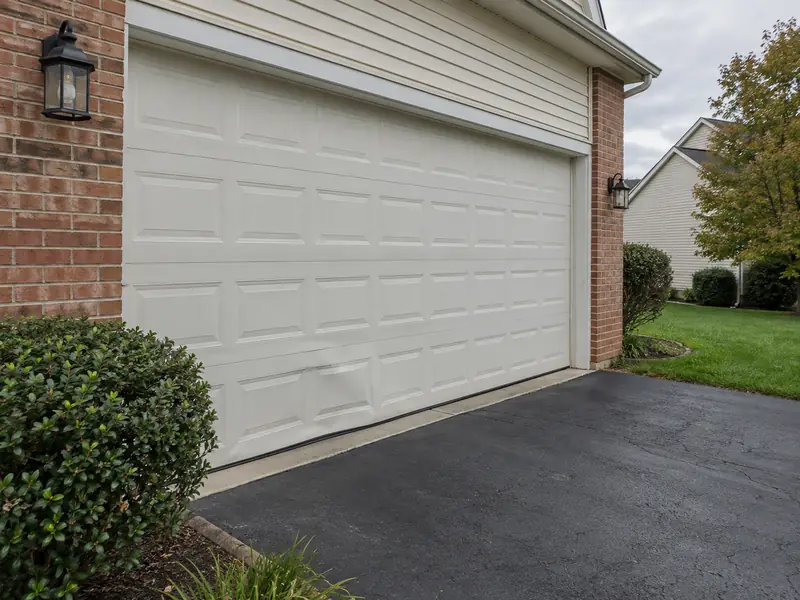 White raised-panel garage door with a dented section on a brick home in Rockville
